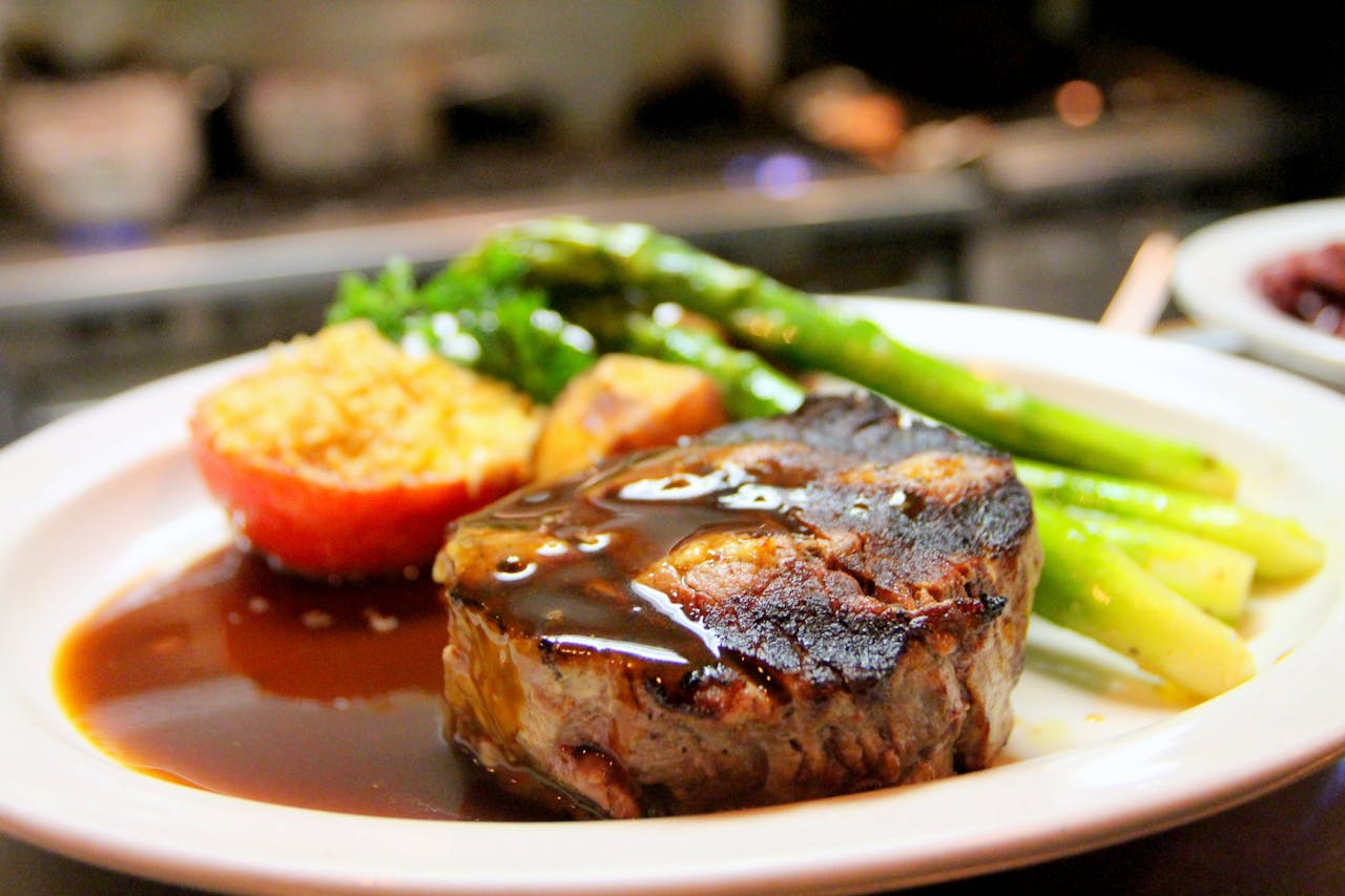 Delicious grilled steak with asparagus and tomato served with rich sauce on a plate.